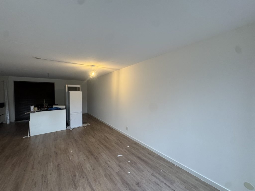 Woonkamer met een houten vloer en strakke witte wanden na het behangen en sauzen